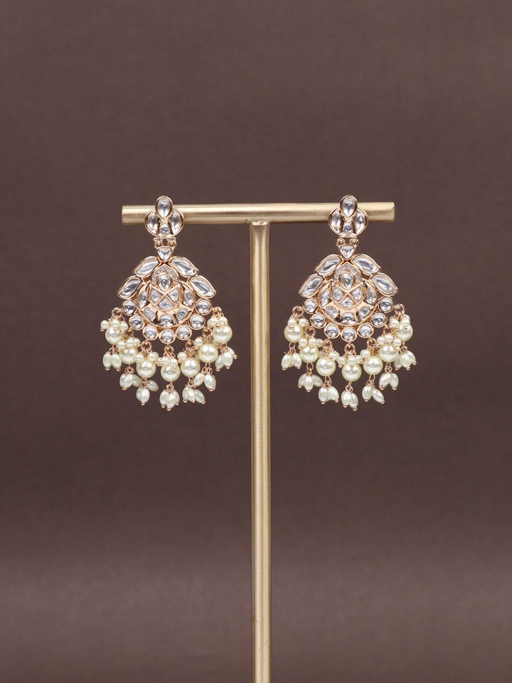 A closeup image of Esha White Kundan Polki Dangler Earrings by Live Some India on a brown background 