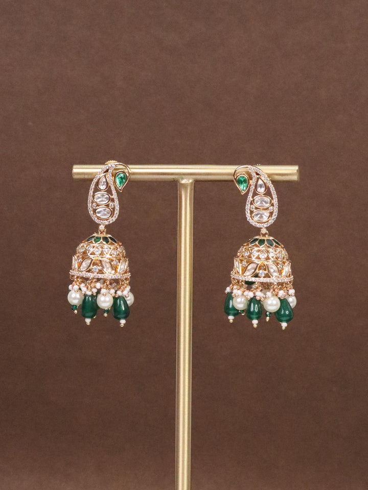 Jodha Kundan Polki & Green Meenakari Jhumka Earrings by Live Some India on a earirng stand with brown background