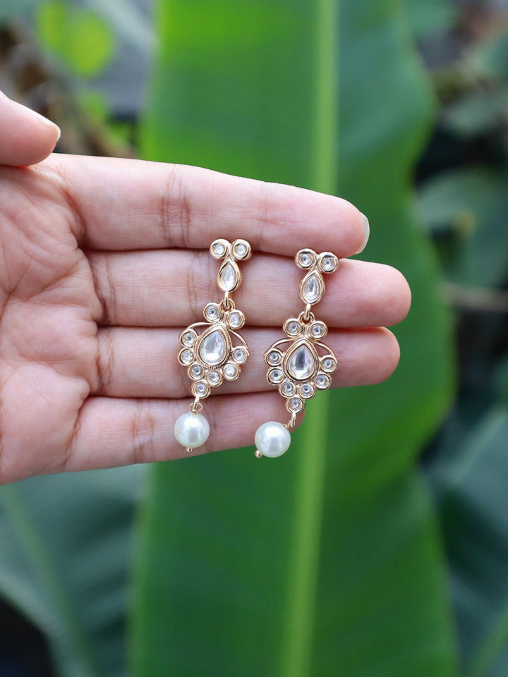 Kundan Polki & Pearls Dangle Earrings on hands with natural green leaves background