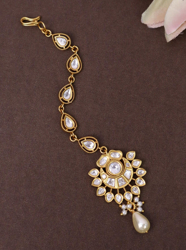 A closeup image of Minimalist Kundan Pearl Maang Tikka by Live Some India on a brown background 