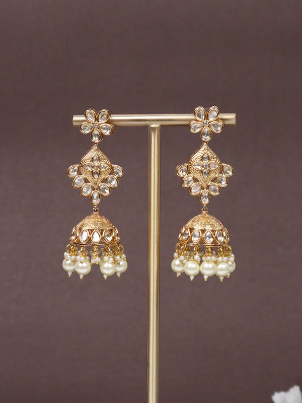 A closeup image of Navras Jhumka Earrings -3 on an earring stand with a brown background and white flowers 