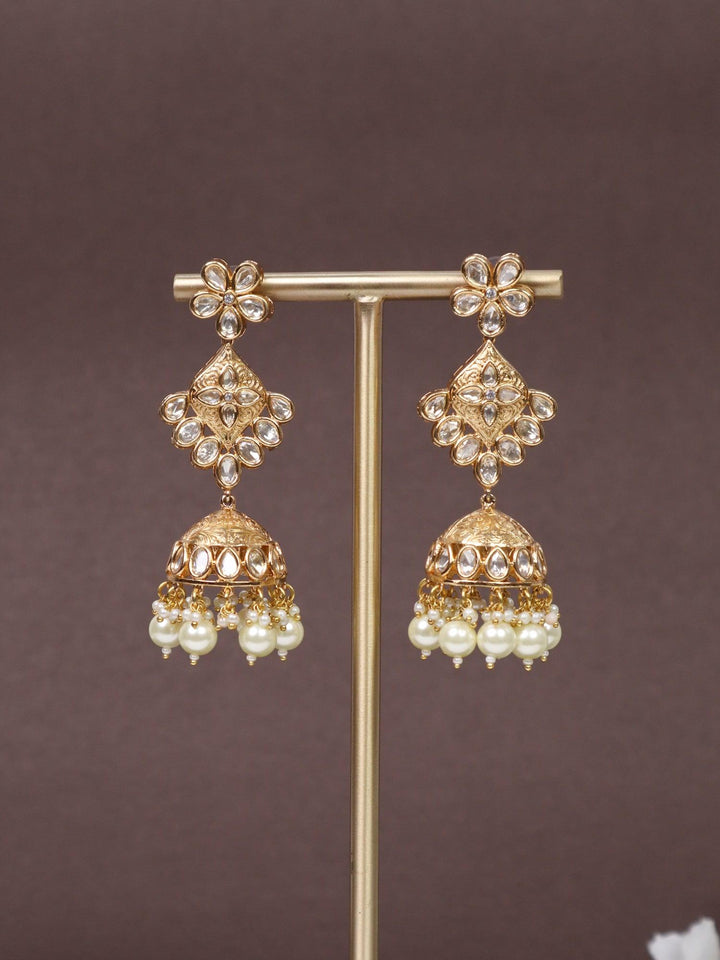 A closeup image of Navras Jhumka Earrings -3 on an earring stand with a brown background and white flowers 