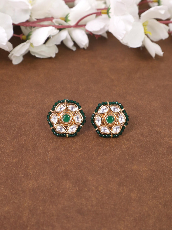 A closeup image of Niva Kundan Polki Green Stud Earrings by Live Some India on a brown background with flowers 