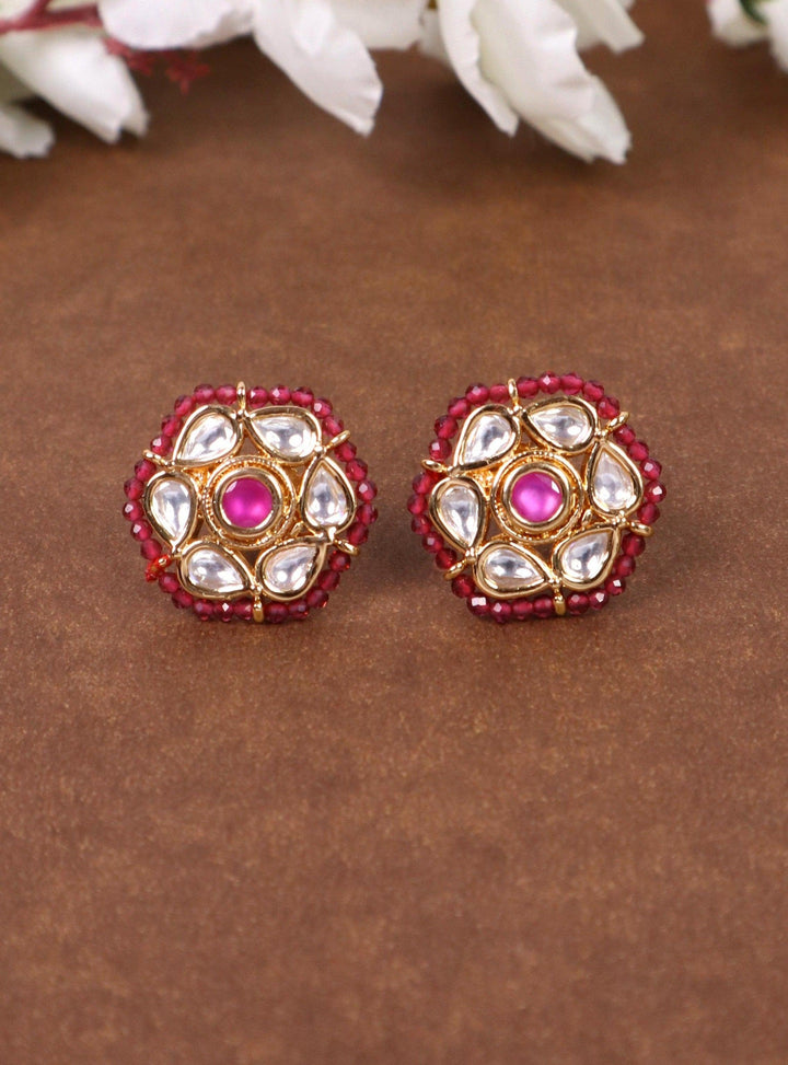 A closeup image of Niva Kundan Polki Stud Earrings by Live Some India on a brown background with flowers