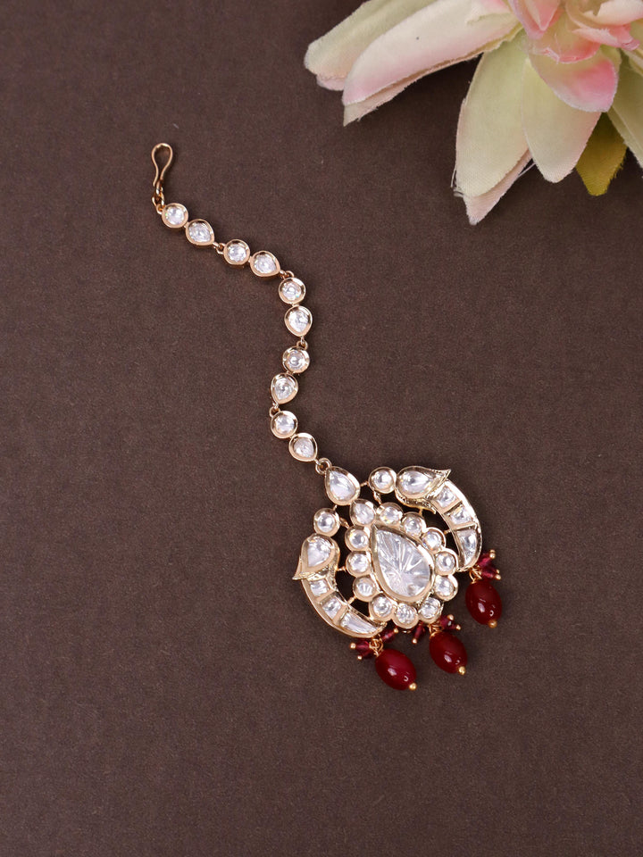 A closeup image of Red Kundan Polki Studded Maang Tikka by Live Some India on a brown background 