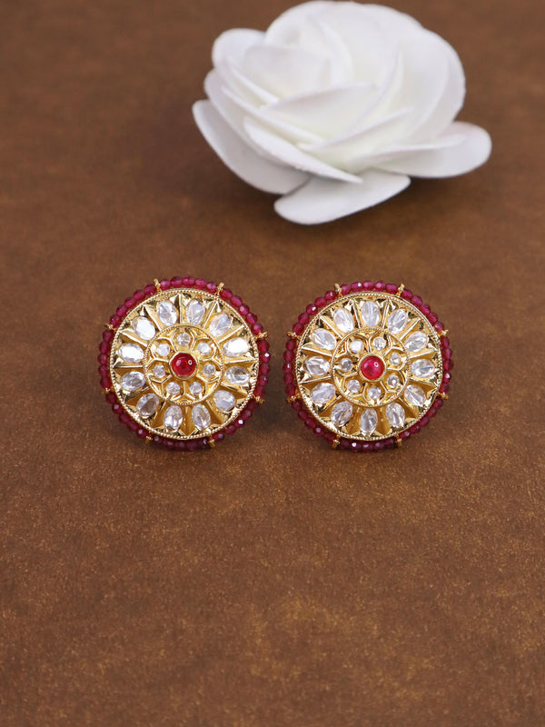 A closeup image of Ria Red Kundan Polki Stud Earrings by Live Some India on a brown background with a white rose