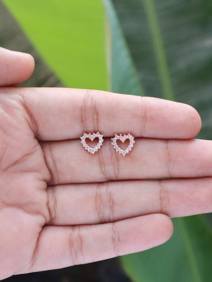 Rose Gold Diamond Heart Earrings by Live Some India on hands with natural green leaves background