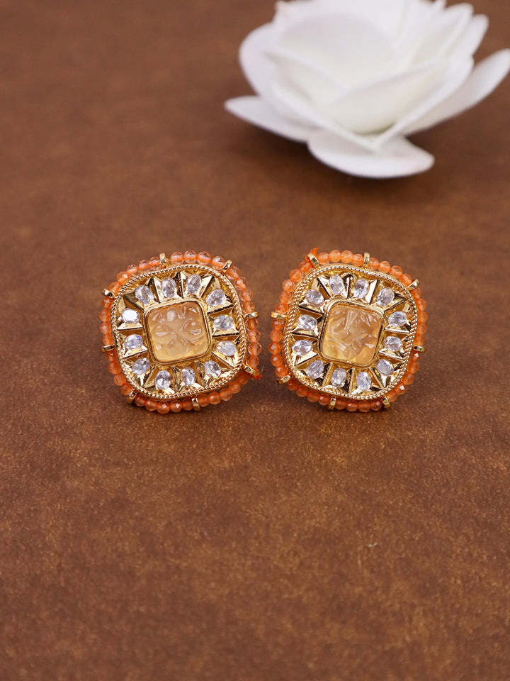 A closeup image of Soft Orange Kundan Polki Stud Earrings by Live Some India on a brown background with a white rose