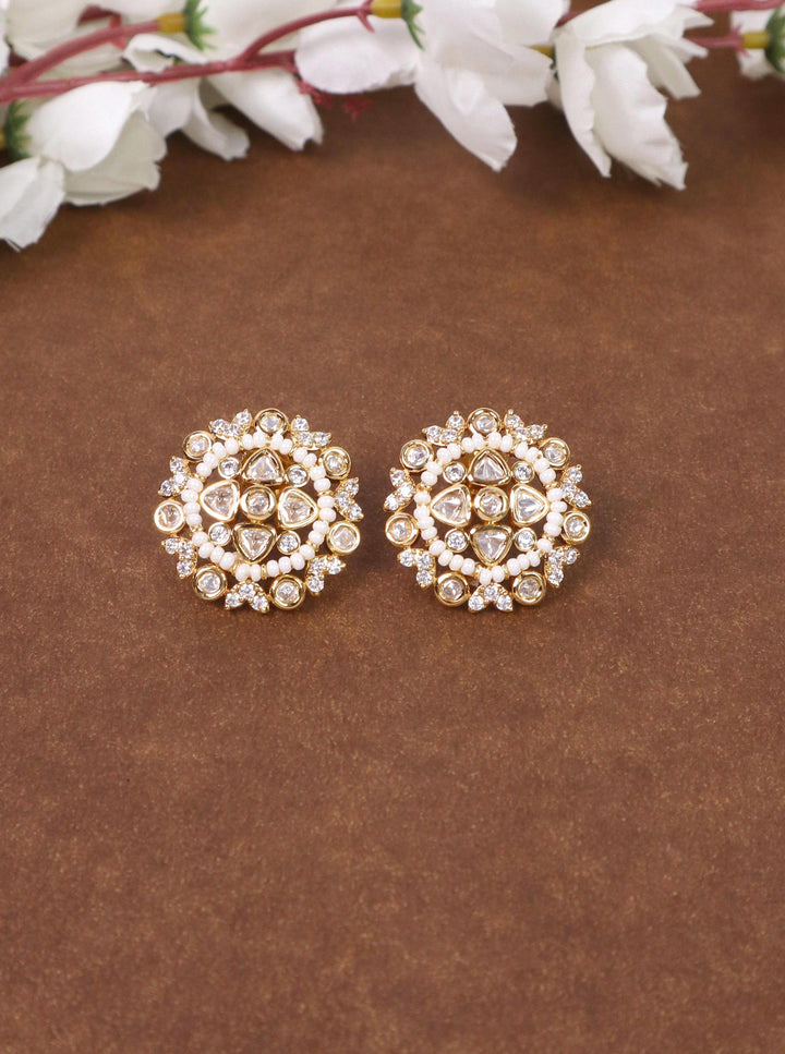 A closeup image of Soni Kundan Polki White Stud Earrings by Live Some India on a brown background with flowers 