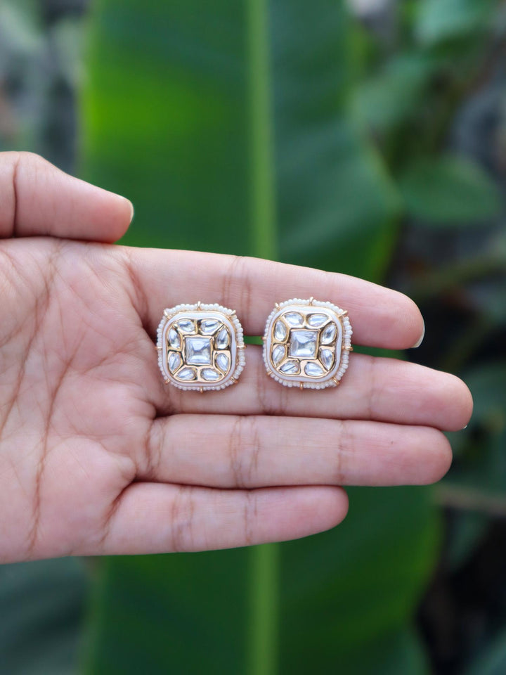 Tanisha Kundan Polki White Stud Earrings by Live Some India on hands with natural green leaves background