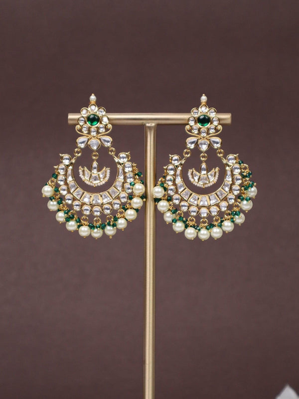 A closeup image of Tara Kundan Polki Chandbali Earrings -2 by Live Some India on an earring stand with a brown background and white flowers 